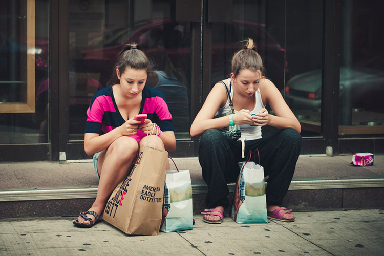 Dos adolescentes sentadas en una acera consultando sus teléfonos móviles