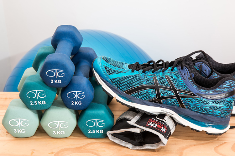 Fotografía de unas pesas y unas zapatillas de deporte, con otros objetos para realizar ejercicio