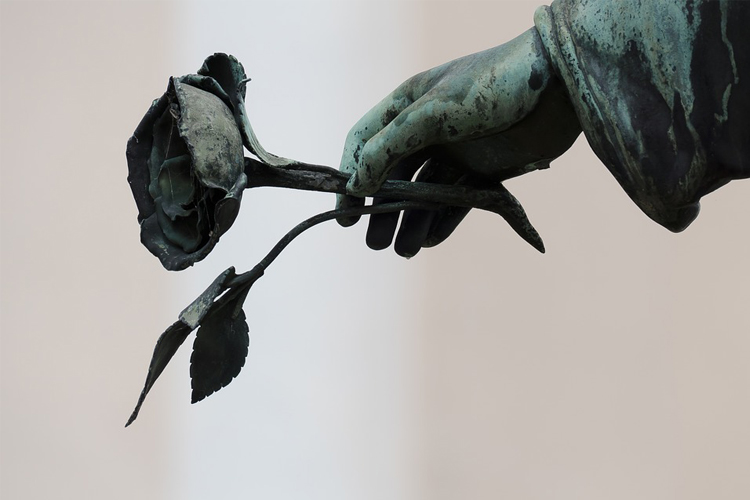 Fotografía de la mano de una estatua que sostiene una rosa.