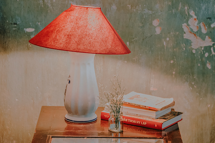 Fotografía de una mesa auxiliar sobre la que hay una lámpara, unos libros y una bote con unas ramitas.
