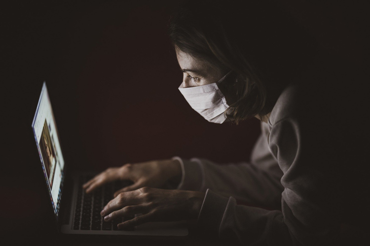 Fotografía de una mujer con mascarilla tecleando un ordenador portátil.