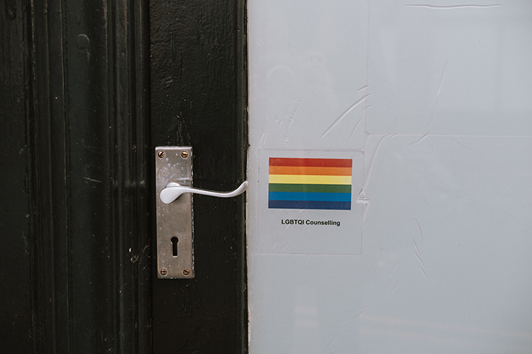 [fotografía] detalle del picaporte de una puerta, junto a un rótulo con la bandera multicolor y la leyenda 'LGTBQ Counseling'