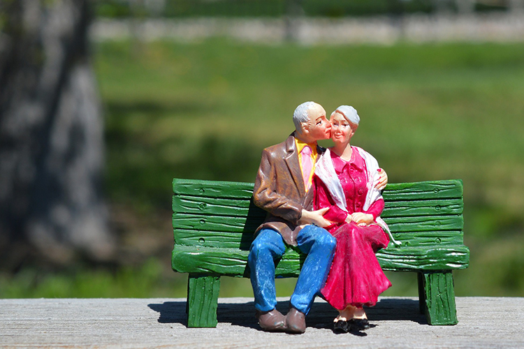 [fotografía] figuras en miniatura de una pareja de ancianos sentados en el banco de un parque en actitud cariñosa