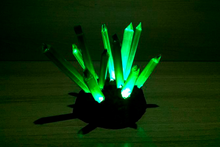 [fotografía] cristales de mineral de color verde dispuestos verticalmente en punta