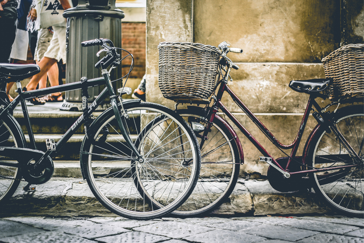 [fotografía] bicicletas de paseo de color negro y cesta portabultos aparcadas junto a una acera