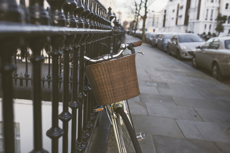 [fotografía] bicicleta de paseo con cesta de mimbre, aparcada junto a una valla