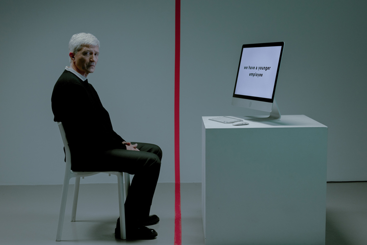 [fotografía] anciano sentado frente a un ordenador con las manos juntas en su regazo