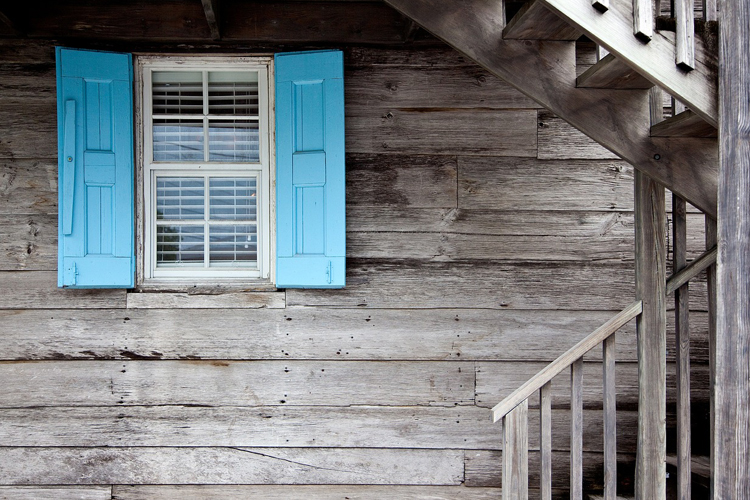 [fotografía] detalle del exterior de una casa vieja de madera con postigos azules en la ventana